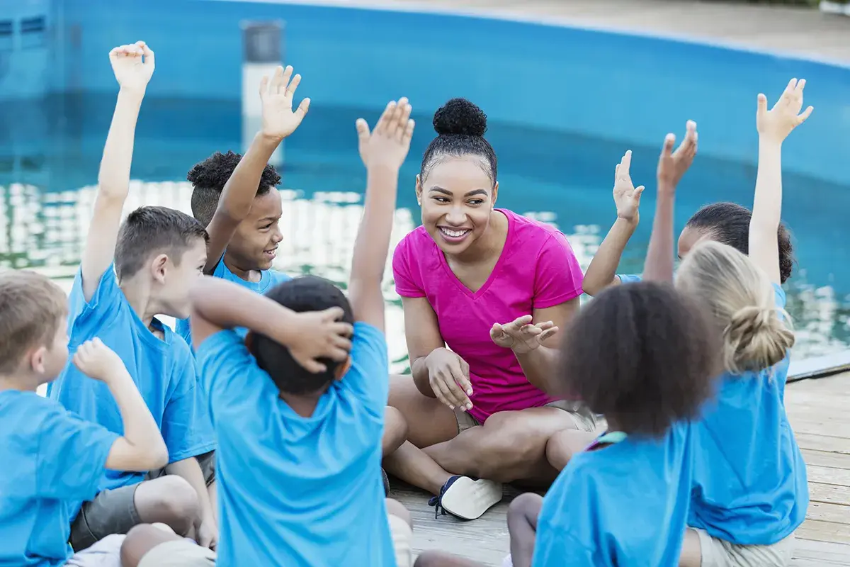 A group of kids wearing matching blue t-shirts sit in a circle with a volunteer docent.
